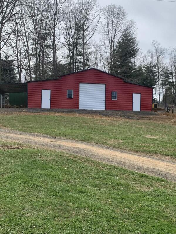 Red metal barn with a roll-up door, two walk-in doors, two windows, and an open lean-to on one side