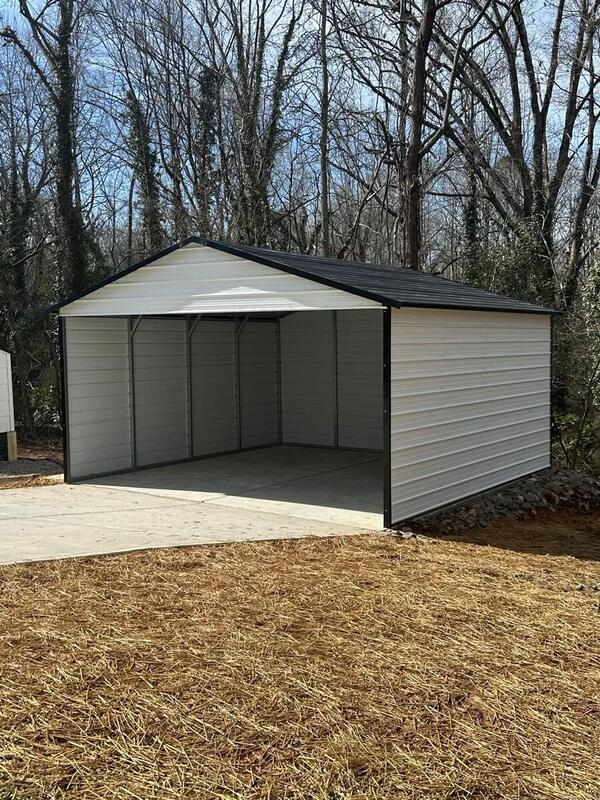 White metal carport with a dark roof, enclosed sides and back, and an open front on a concrete pad