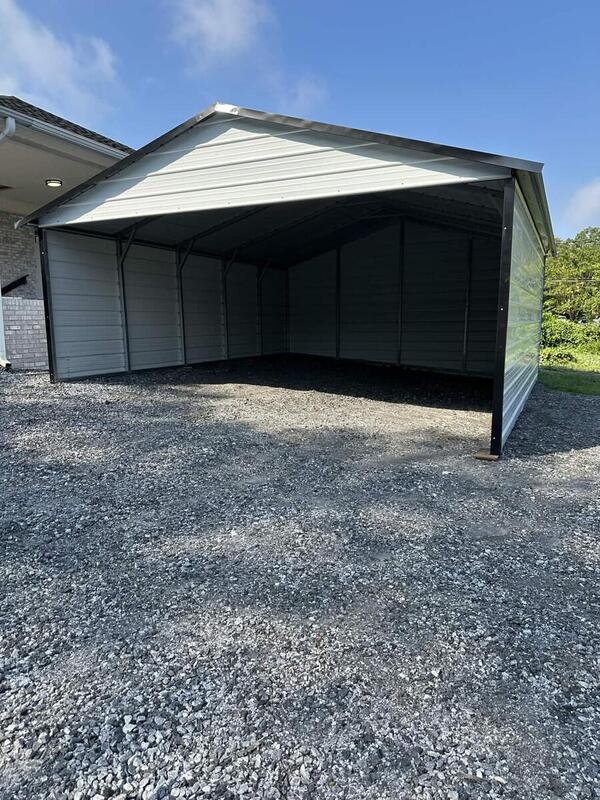 White metal carport with black trim, enclosed sides and back, and an open front on gravel