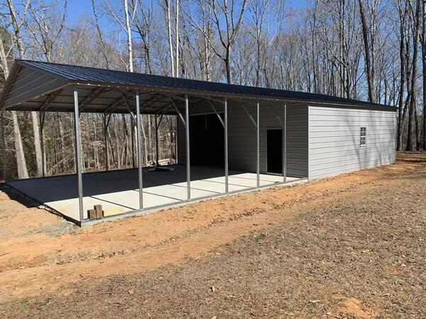 Long open-sided metal carport over a concrete slab with an enclosed storage room at the back