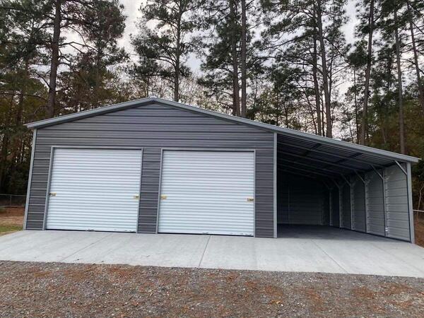 Dark gray metal garage with two white roll-up doors and a side lean-to with enclosed walls, on a concrete slab