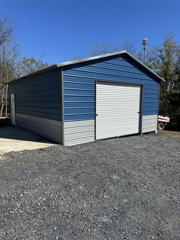 Blue metal garage with light gray lower panels and a white roll-up door, on gravel