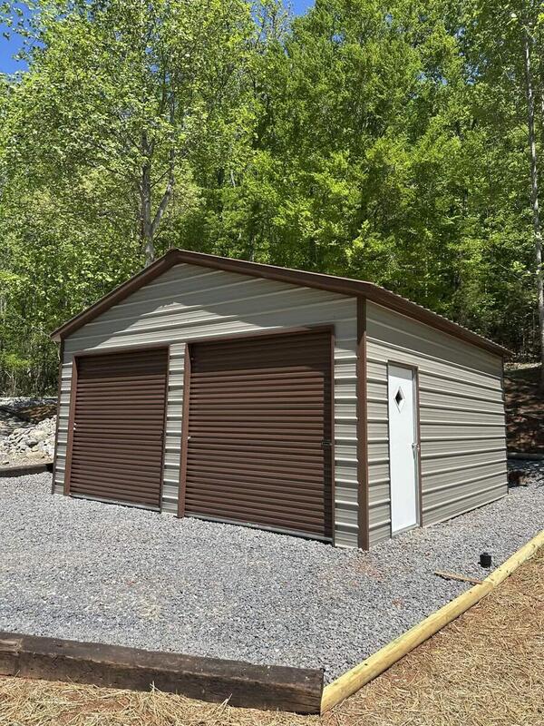 Tan metal garage with brown trim, two brown roll-up doors, and a walk-in door, on a gravel pad