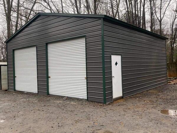 Dark gray metal garage with green trim, two white roll-up doors, and a walk-in door